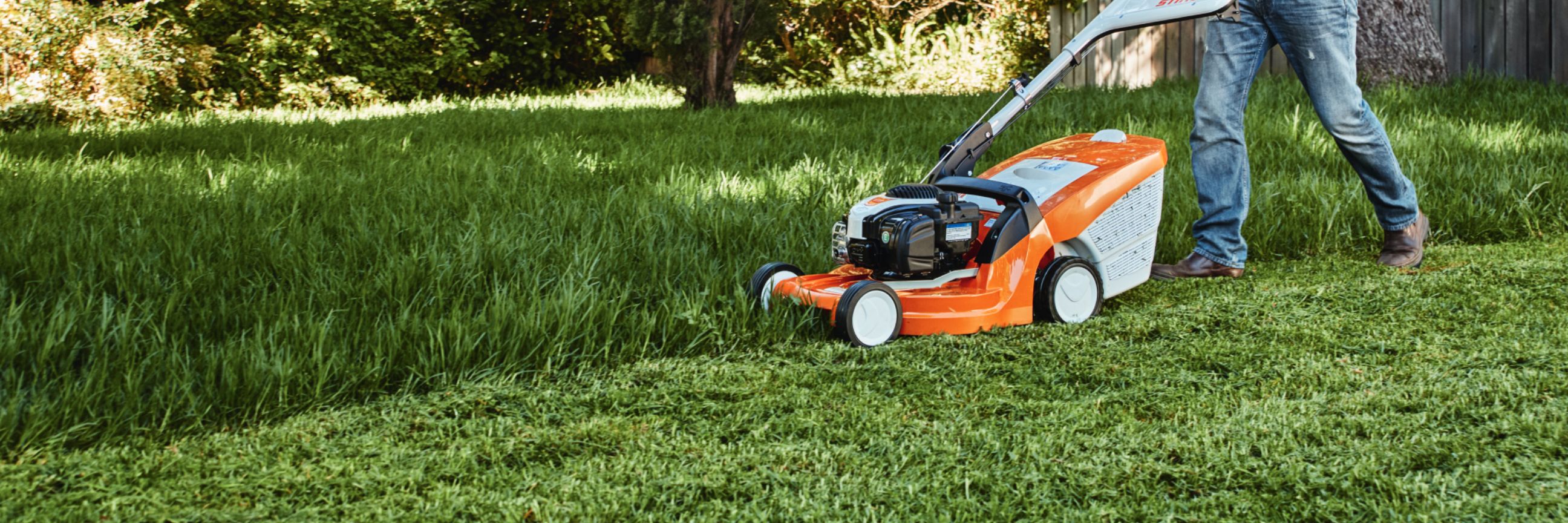 Person mäht hohes Gras mit Rasenmäher